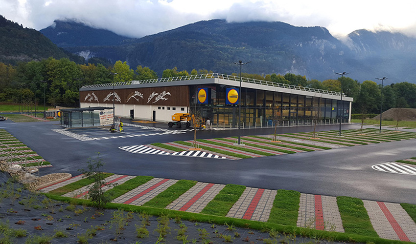ECORASTER Bloxx Parkplätze eines Supermarktes vor Bergkulisse.
