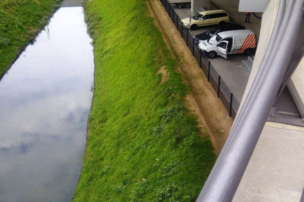 Begrüntes Wassersammelbecken mit parkenden Autos an der Seite