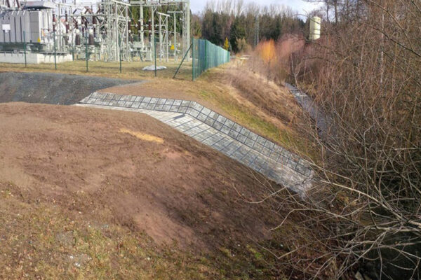 Wasserüberlauf mit ECORASTER Bloxx befestigt und Büschen und Industrieanlagen im Hintergrund