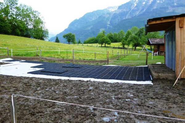 Verlegung von ECORASTER auf Vliesschicht, um Paddock schlammfrei zu machen. Bergpanorama im Hintergrund