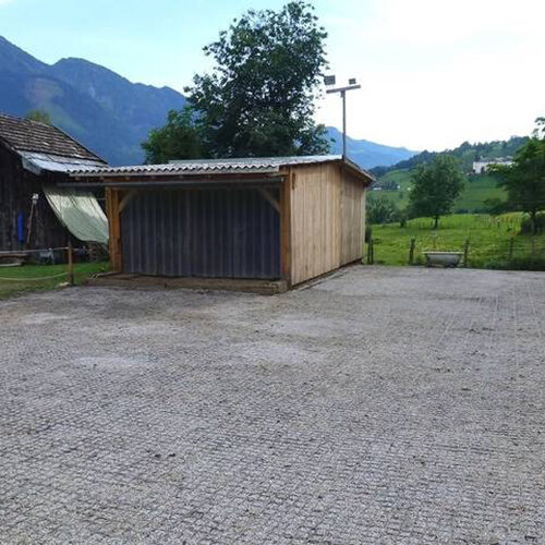 Fertige Paddock Fläche mit befüllten ECORASTER Bodengittern und kleinem Stall. Berge und Grünlandschaft im Hintergrund.