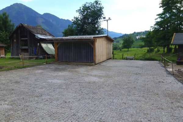 Fertige Paddock Fläche mit befüllten ECORASTER Bodengittern und kleinem Stall. Berge und Grünlandschaft im Hintergrund.