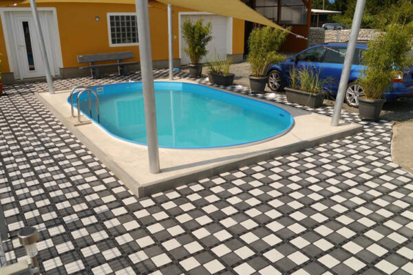 Poolaußenfläche mit ECORASTER Bloxx verlegt, gelbes Haus und blaues Auto im Hintergrund