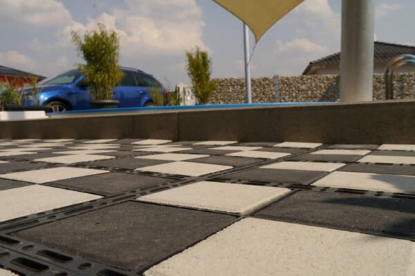 Detailansicht einer ECORASTER Bloxx Fläche in Schachbrett Muster und mit blauem Auto im Hintergrund