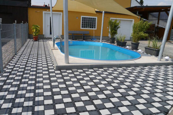 ECORASTER Bloxx Fläche für Außen- und Poolbereich, im Hintergrund ein gelbes Haus
