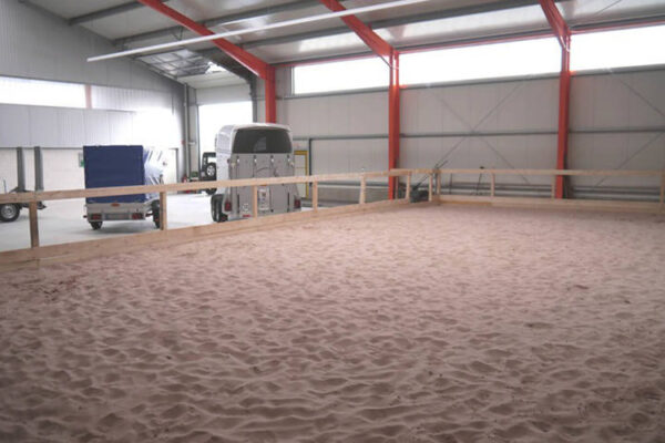 Sandiger Reithallenboden mit Pferdeanhänger im Hintergrund