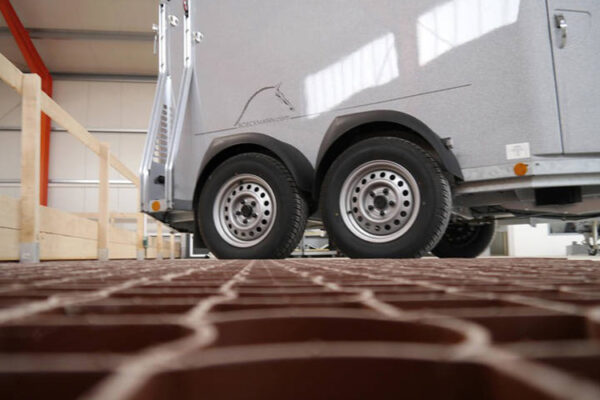 Detailansicht von unbefüllten terrakottafarbigen ECORASTER Bodengittern mit Pferdeanhänger im Hintergrund