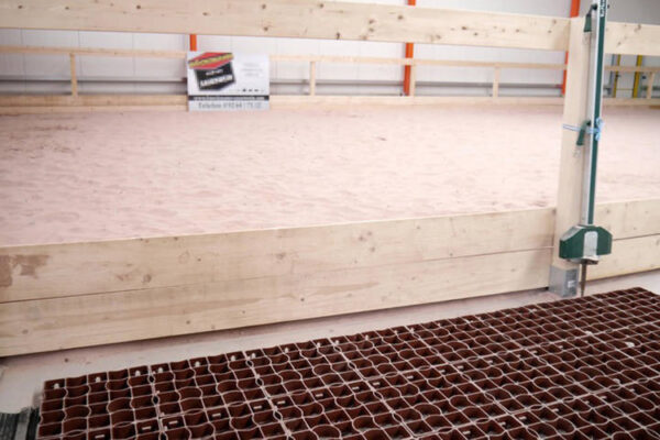 Unbefüllte terrakottafarbige ECORASTER liegen neben sandigem Boden einer Reithalle
