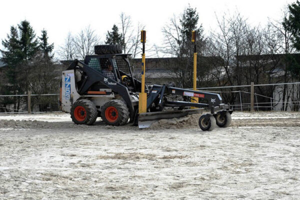 Maschine bearbeitet die sandige Oberfläche eines Reitplatzes