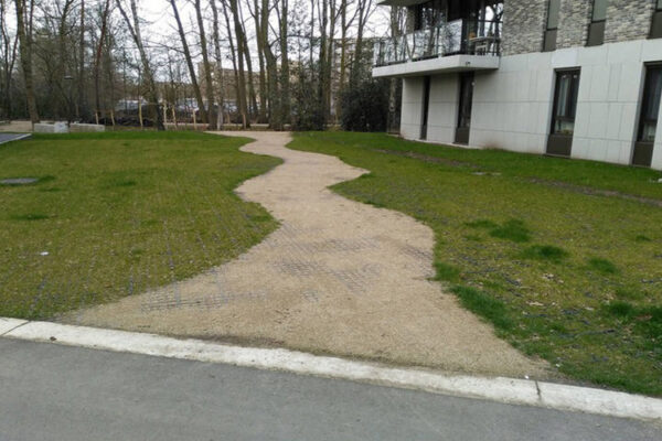 Rasenfläche und Sandweg mit ECORASTER befestigt. Wohnanlage und Bäume im Hintergrund