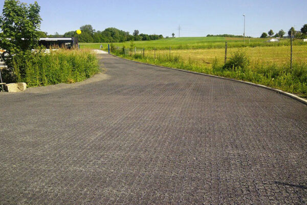 Mit Splitt verfüllte Fläche einer Einfahrt, im Hintergrund grüne Landschaft und Bäume