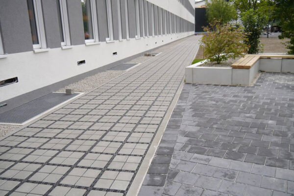 Zufahrt_Selb_03_800x500px Weg aus ECORASTER Bloxx entlang eines Firmengebäudes mit Sitzmöglichkeiten und Büschen am Rand